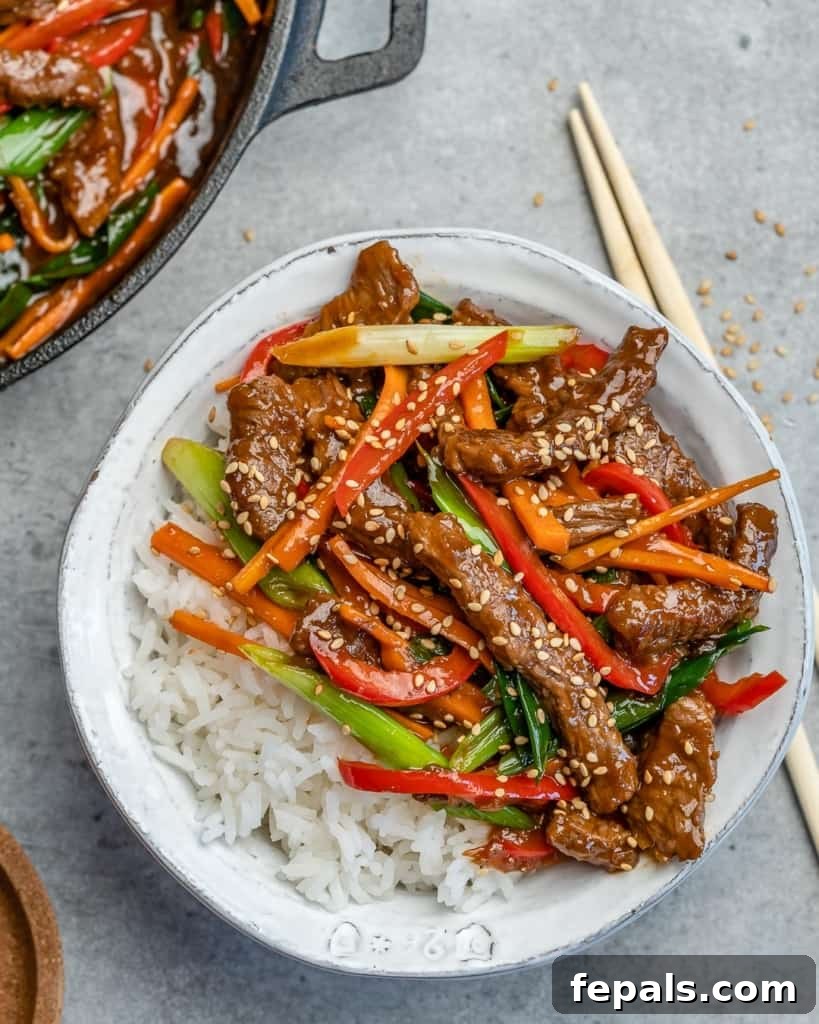 Close-up of chopsticks next to a white bowl filled with savory beef stir fry and fluffy rice, ready to be enjoyed.