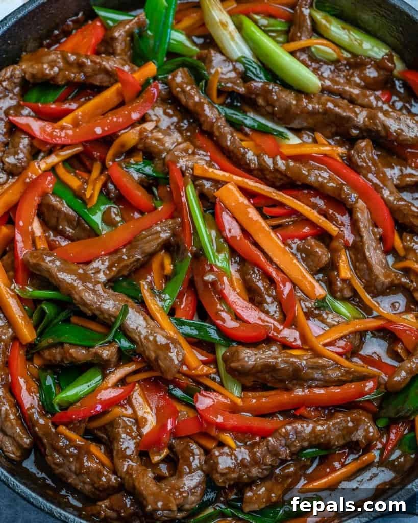 Close-up view of a vibrant beef stir fry with carrots, red bell peppers, and green onions, glistening with sauce.