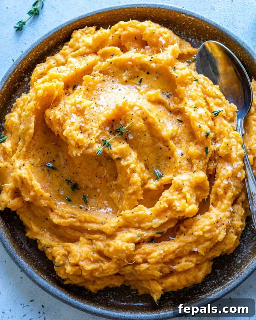 Velvety Sweet Potato Mash 3 A close-up view of creamy mashed sweet potatoes in a bowl, with a spoon digging into its luscious texture, highlighting the deliciousness and smooth consistency.