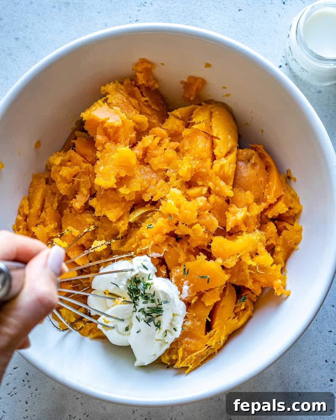 Velvety Sweet Potato Mash 6 A bowl of mashed sweet potato with a side of cream cheese being whisked, illustrating the creamy texture and the key ingredient for this healthy recipe.