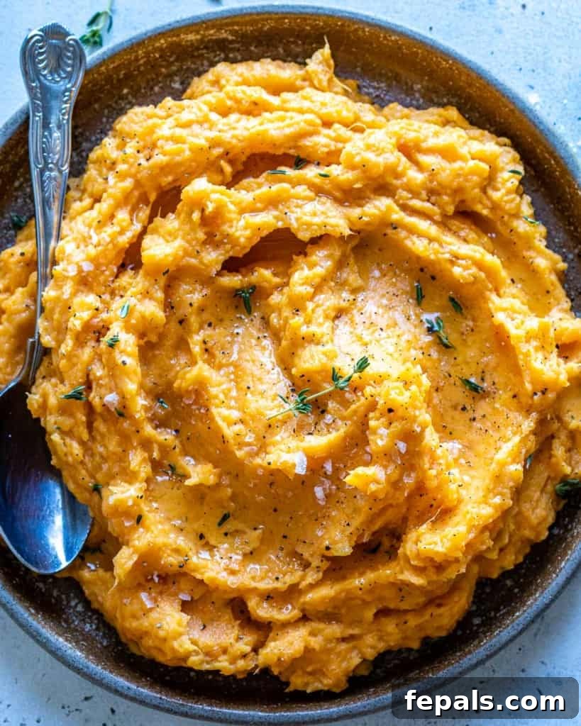 Velvety Sweet Potato Mash 7 A top-down view of a generously portioned bowl of mashed sweet potatoes, garnished with fresh herbs and a hint of olive oil, with a serving spoon nestled in, inviting a delicious taste.