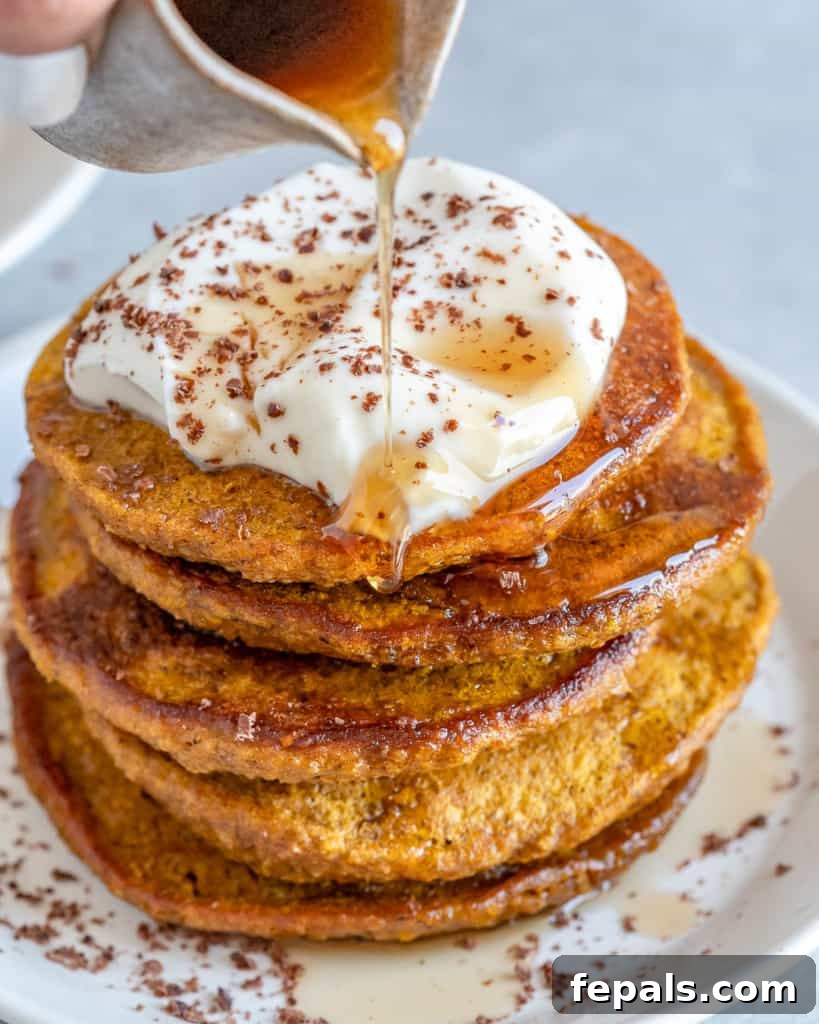 easy pumpkin pancakes with yogurt topping and maple being drizzled over the pancakes
