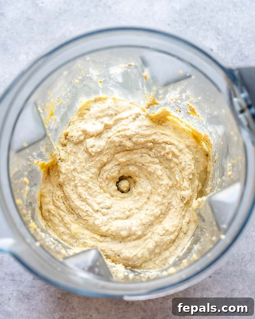 A close-up view of the tofu and cashew filling being processed until smooth and creamy in a food processor, ready to be layered into the lasagna.