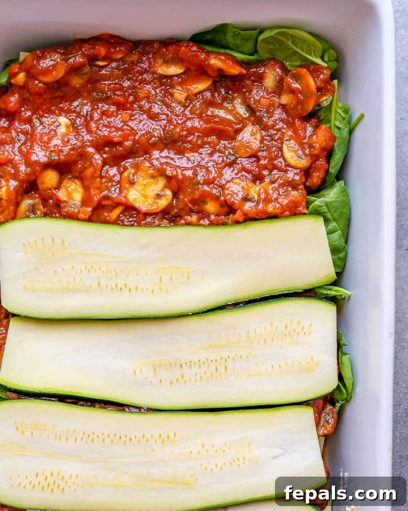A visual of the lasagna assembly process, showing partial layers of vibrant zucchini and rich marinara sauce nestled in a baking dish, preparing for the next delicious layer.