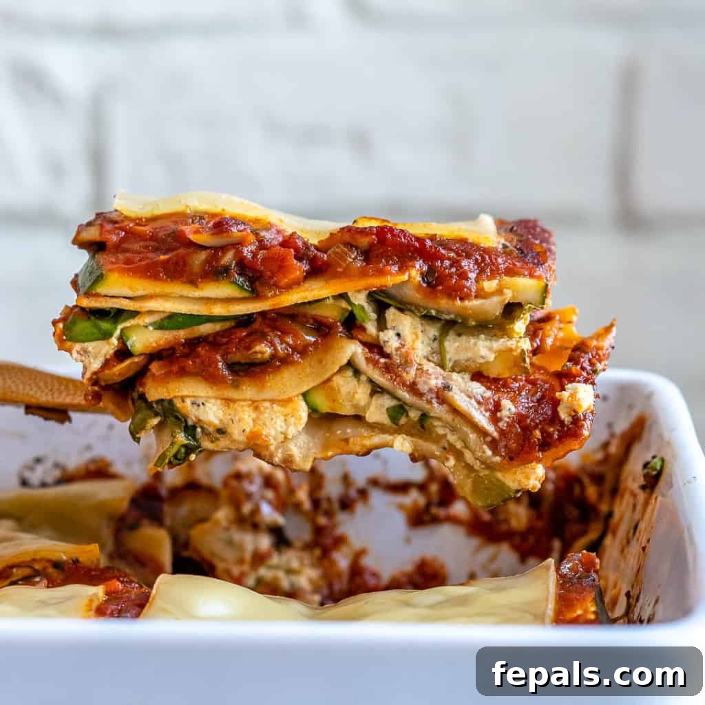 A kitchen spatula carefully lifting a perfectly cooked slice of vegan zucchini lasagna out of a baking pan, ready to be served and enjoyed.