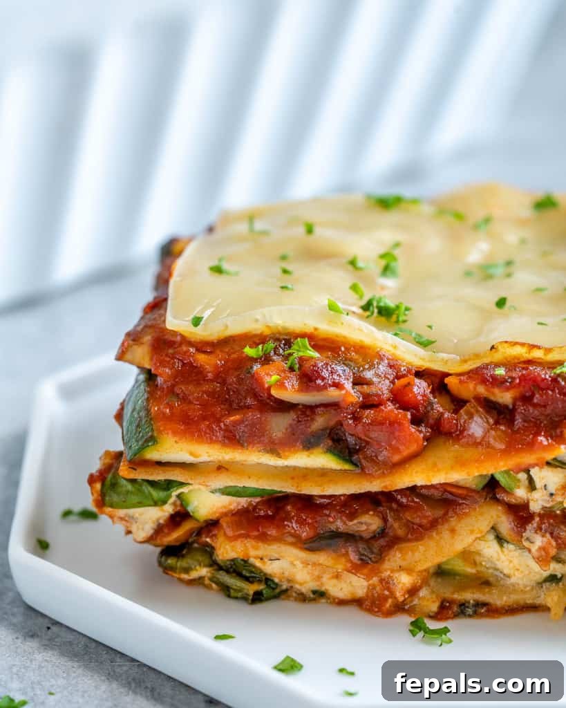 A close-up view of a single slice of vegan zucchini lasagna served on a pristine white plate, highlighting its vibrant layers and inviting texture.