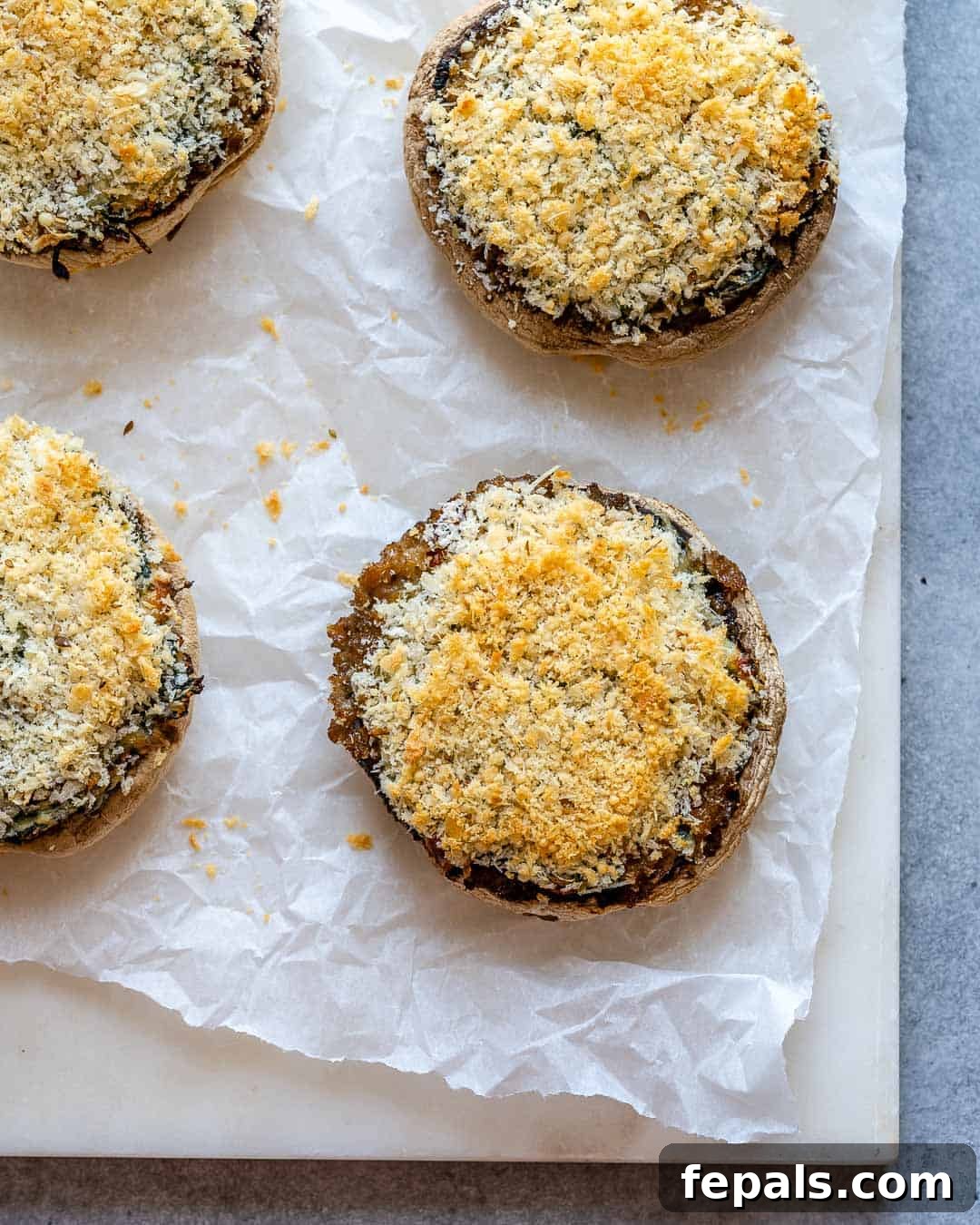 Rustic Tuscan Stuffed Mushrooms 8 An overhead shot of an oven-safe sheet pan lined with parchment paper, holding several perfectly golden-brown Tuscan stuffed mushrooms, fresh and steaming.