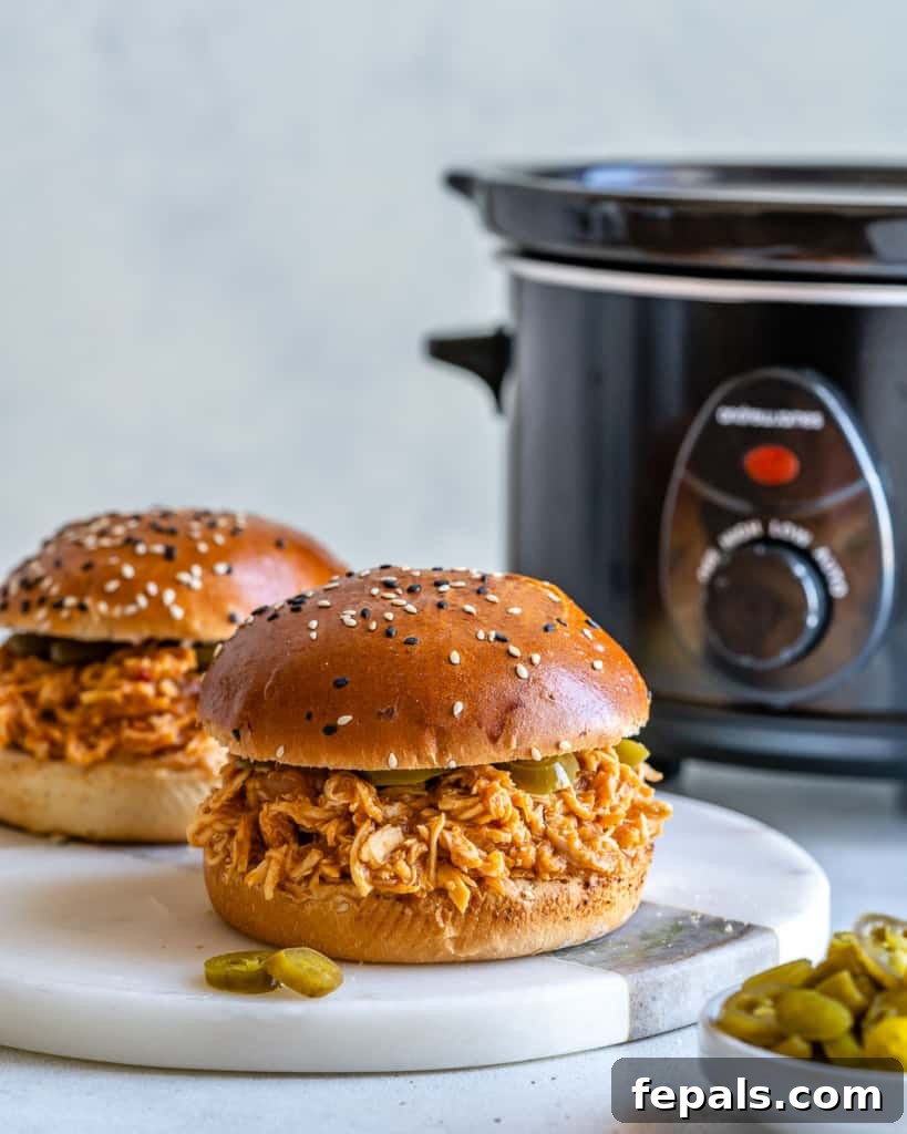 Two pulled chicken burgers with slow cooker in the background 