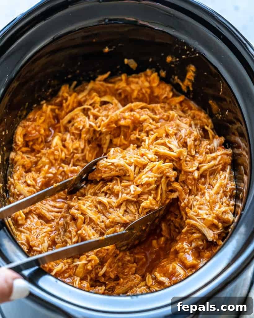 Top view of Crockpot filled with pulled chicken and tongs