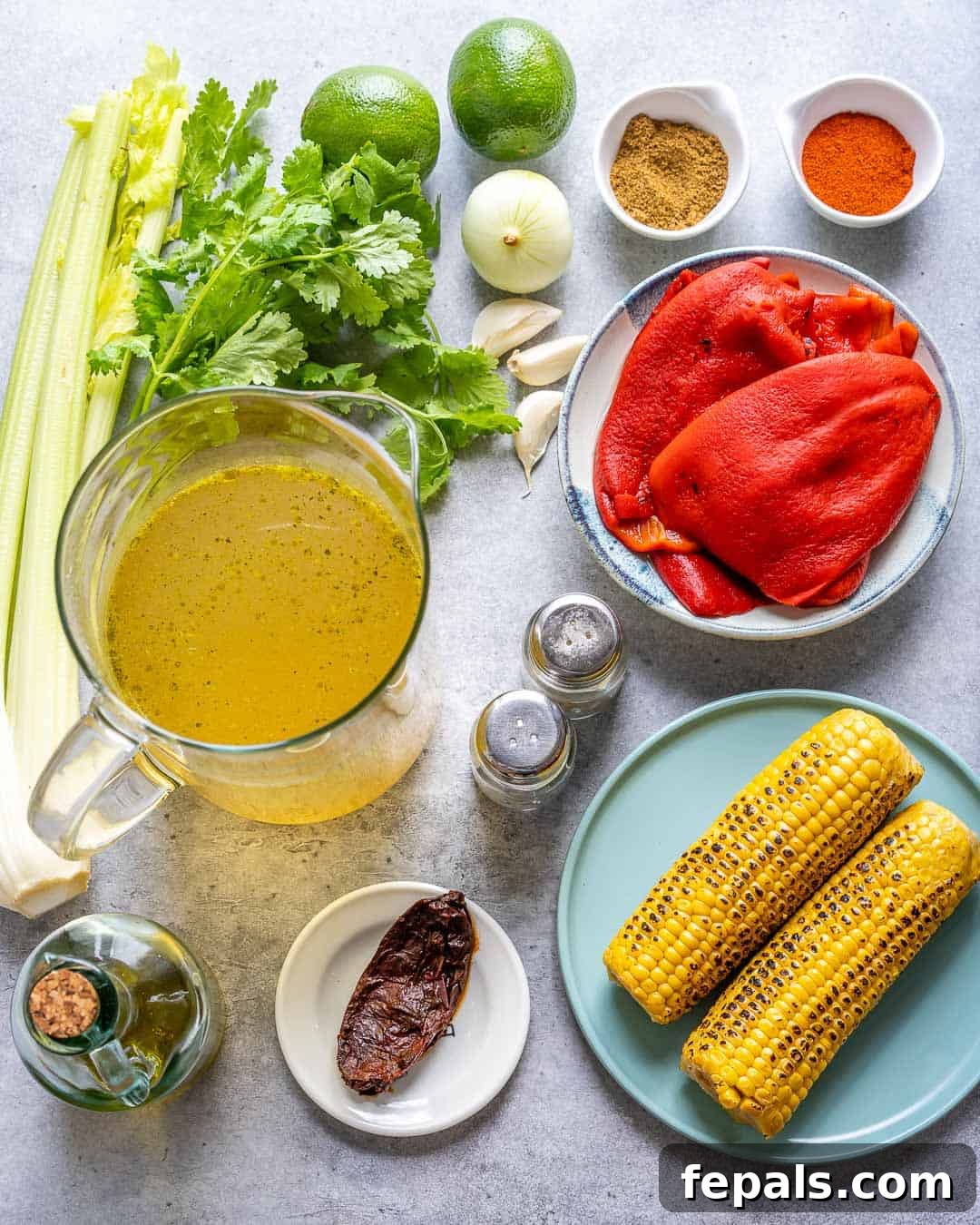 Creamy Mexican Street Corn Soup 4 A vibrant flat lay of all the fresh ingredients needed for Mexican Sweet Corn Soup: corn cobs, chipotle peppers, olive oil, vegetable broth, salt, pepper, red peppers, cilantro, celery, limes, garlic, onion, cumin, and paprika.