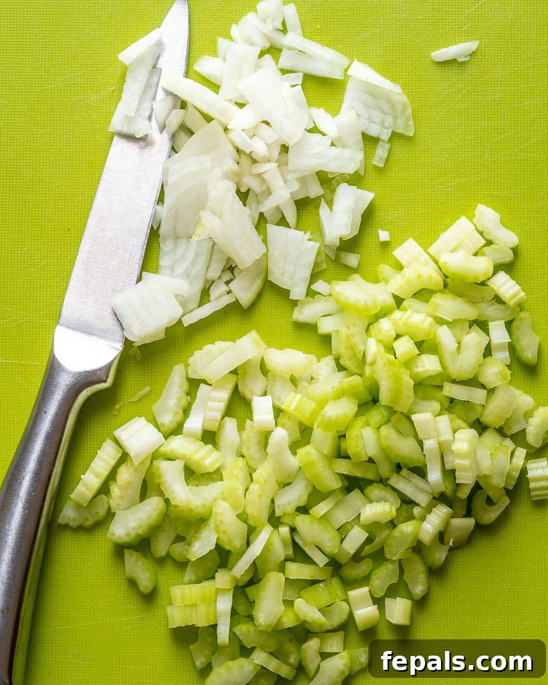 Creamy Mexican Street Corn Soup 5 A person expertly chopping celery with a knife on a wooden cutting board, highlighting the fresh preparation for Mexican Sweet Corn Soup.