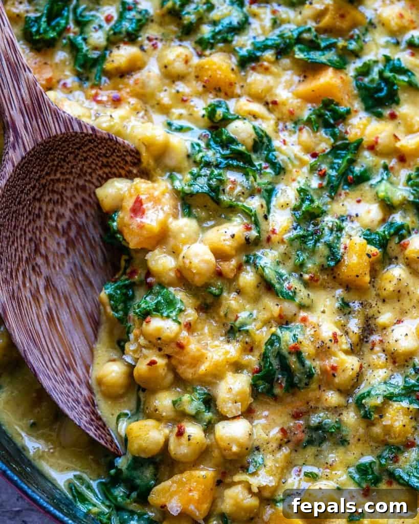 Close-up of spoon stirring a chickpea and butternut squash curry. in a skillet