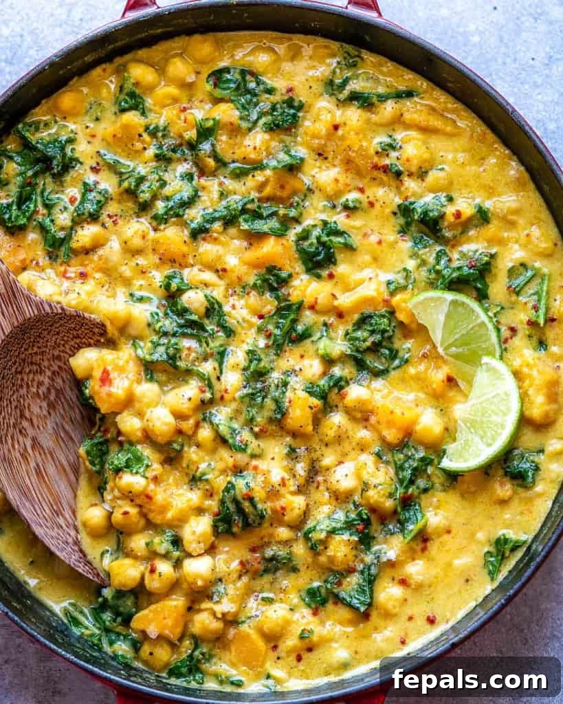 Overhead view of chickpea butternut squash curry in a pot being stirred with a wooden spoon