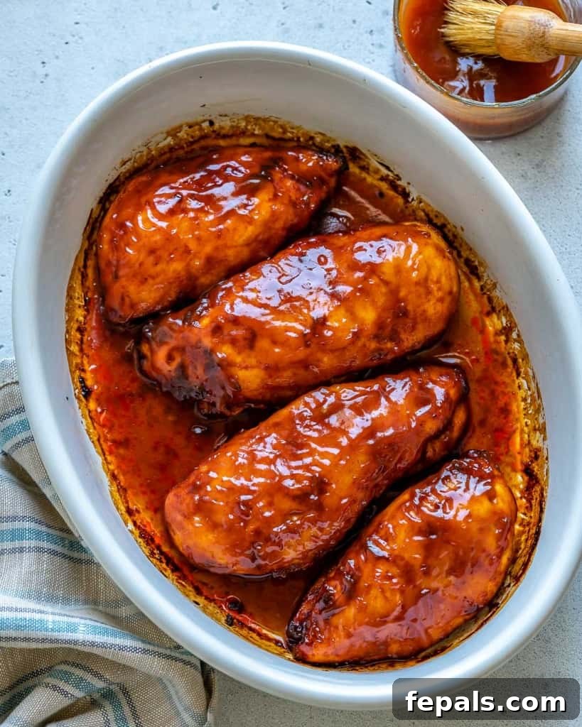 Glazed BBQ Chicken Breast 2 Top view of white baking dish with 4 Baked BBQ Chicken Breasts and bowl of BBQ sauce on side