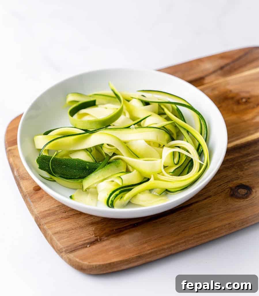 Simple Steps to Homemade Zucchini Noodles 2 side shot of zoodles in a white plate over a brown cutting board, garnished with fresh herbs