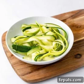 side shot of zoodles in a white plate over a brown cutting board
