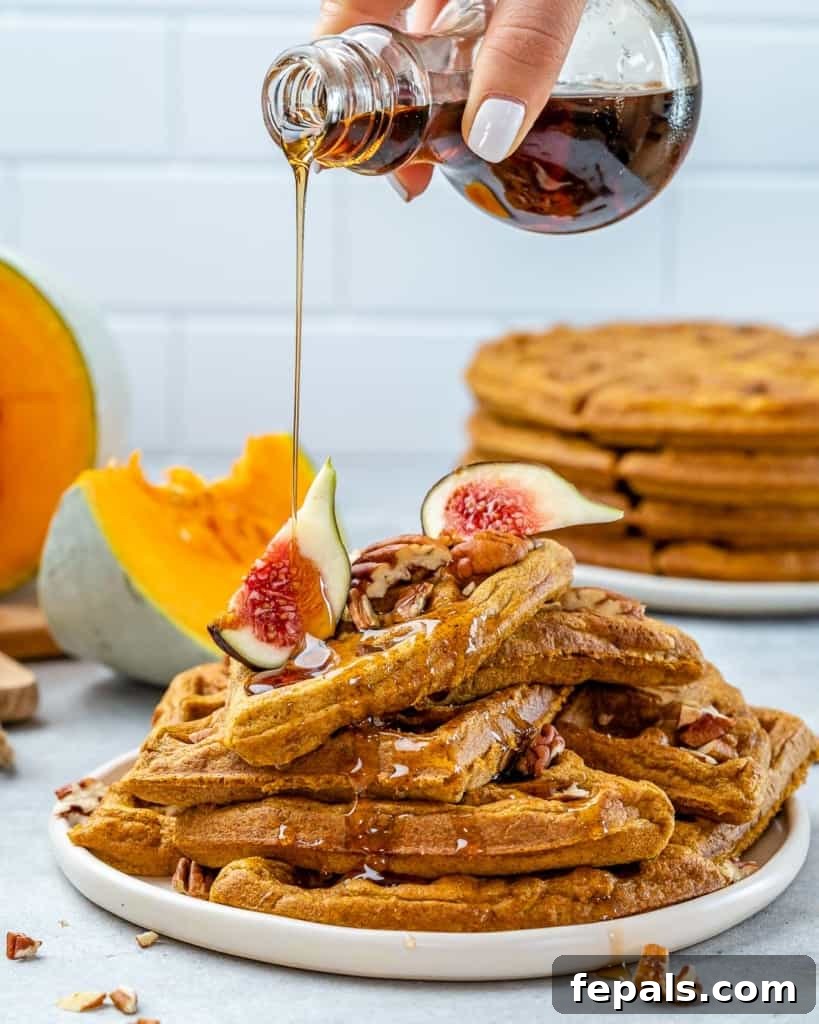 Wholesome Pumpkin Waffles 3 Close-up of a hand pouring rich maple syrup over a stack of golden brown pumpkin waffles, steam rising, suggesting warmth and freshness.