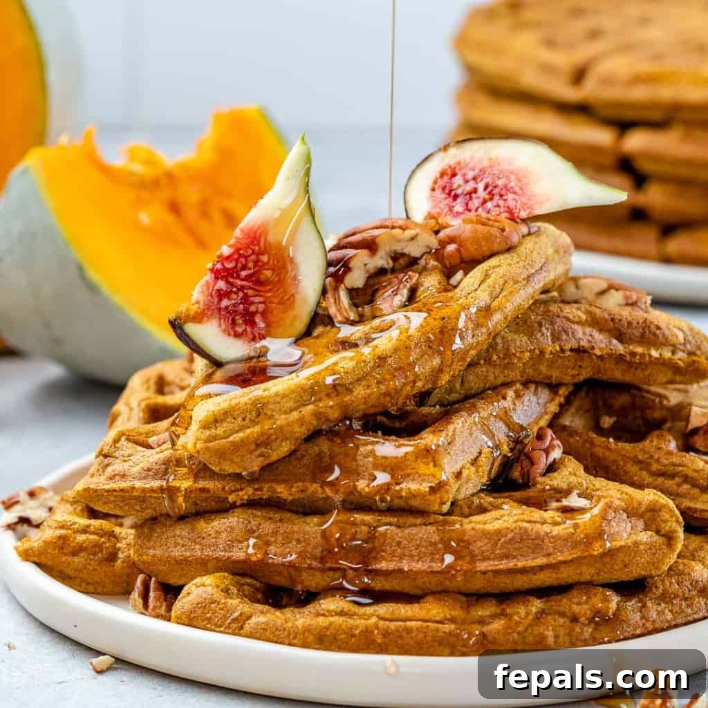 Wholesome Pumpkin Waffles 8 A close-up side shot of a stack of golden pumpkin waffles on a white plate, with a generous stream of maple syrup being drizzled over them.
