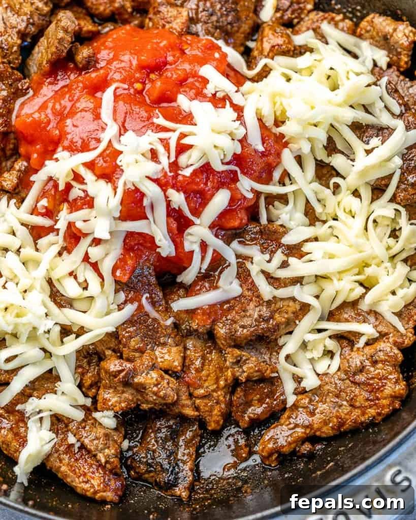 Fiesta Keto Steak Stuffed Peppers 6 Overhead view of steak, shredded cheese, and diced tomatoes mixing in a skillet, creating the vibrant filling.