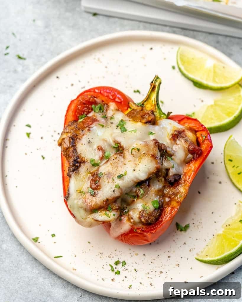 Fiesta Keto Steak Stuffed Peppers 7 Overhead view of a perfectly baked, cheese-topped stuffed pepper on a plate with fresh lime wedges.