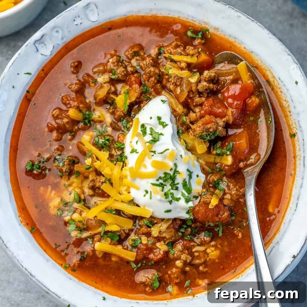 Ultimate Keto Beef Chili 2 Top down view of keto beef chili in a white bowl, garnished with fresh herbs and cheese.