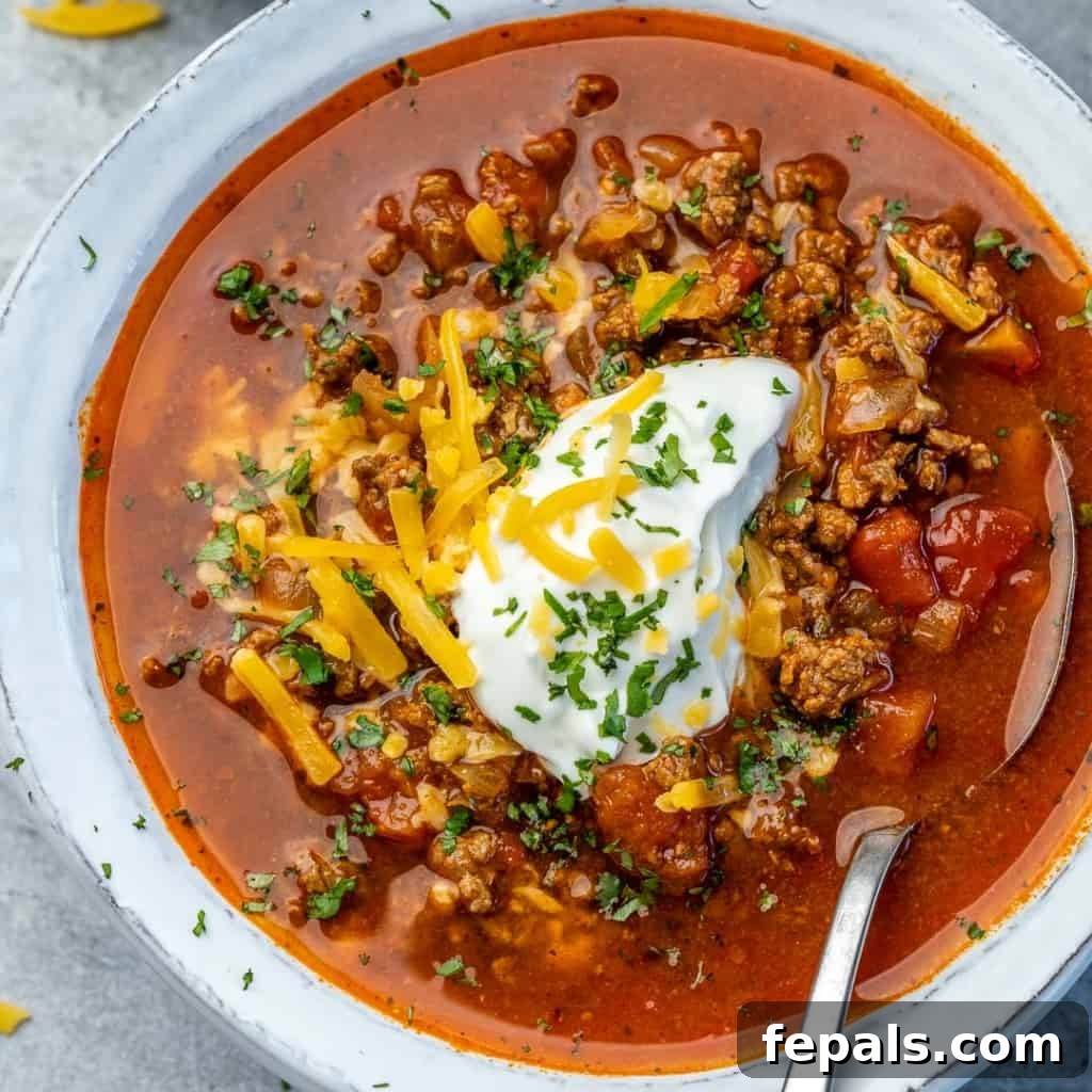Ultimate Keto Beef Chili 3 Close-up top view of keto beef chili in a white bowl with a spoon, showing rich texture and toppings.