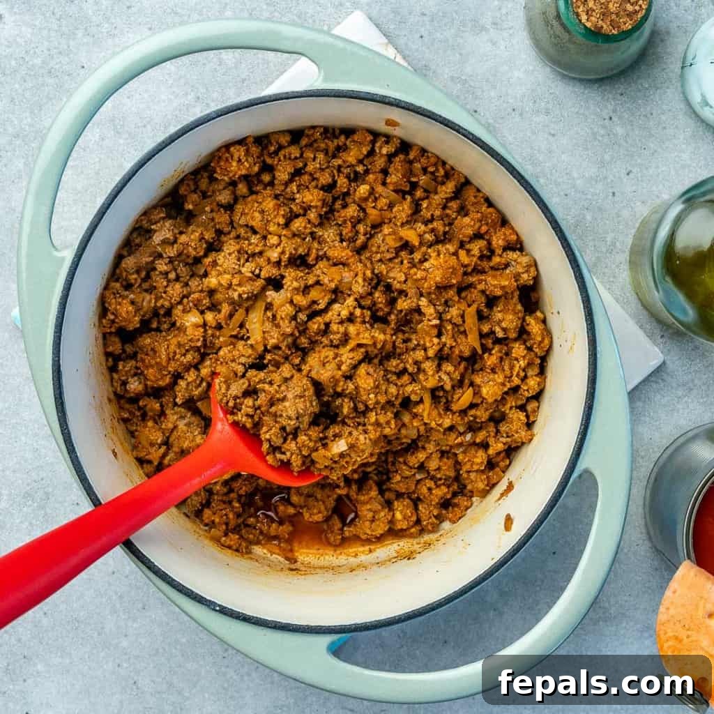 Ultimate Keto Beef Chili 5 Top down view of ground beef browning with spices in a blue Dutch oven.