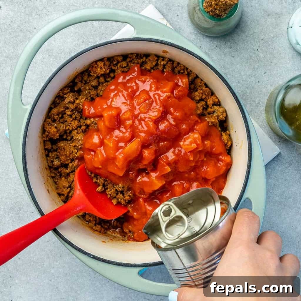 Ultimate Keto Beef Chili 6 Diced tomatoes and ground beef simmering together in a blue pot, adding rich color.