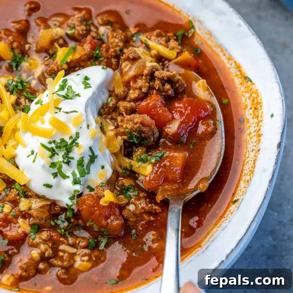 Ultimate Keto Beef Chili 8 A spoon emerging from a blue pot filled with rich, simmering keto beef chili.