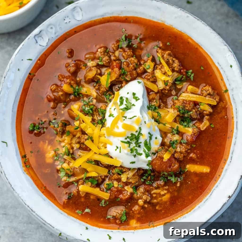 Ultimate Keto Beef Chili 9 Overhead view of keto beef chili in a white bowl, topped with shredded cheese and a dollop of sour cream.
