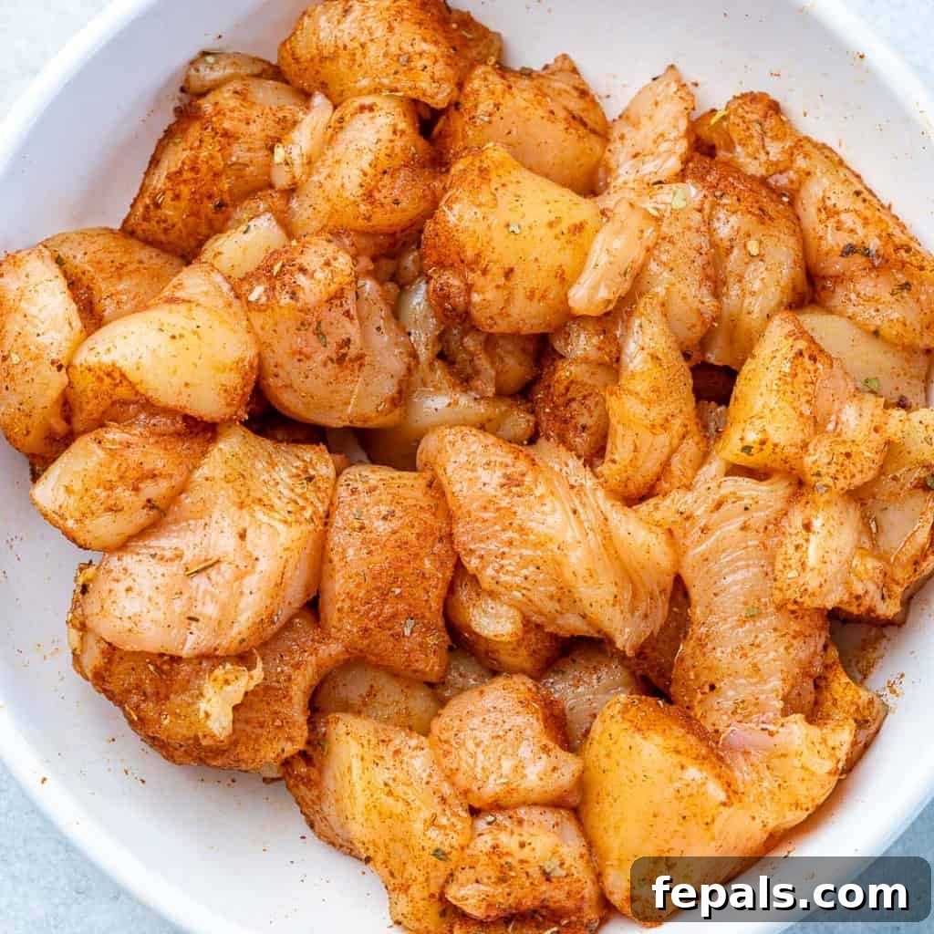 Raw chicken bites seasoned with lime and taco seasoning in a white bowl, ready for cooking