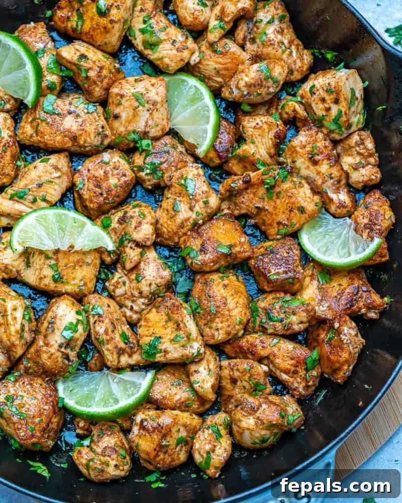 Overhead view of a cast-iron skillet filled with cilantro lime chicken bites and fresh lime wedges