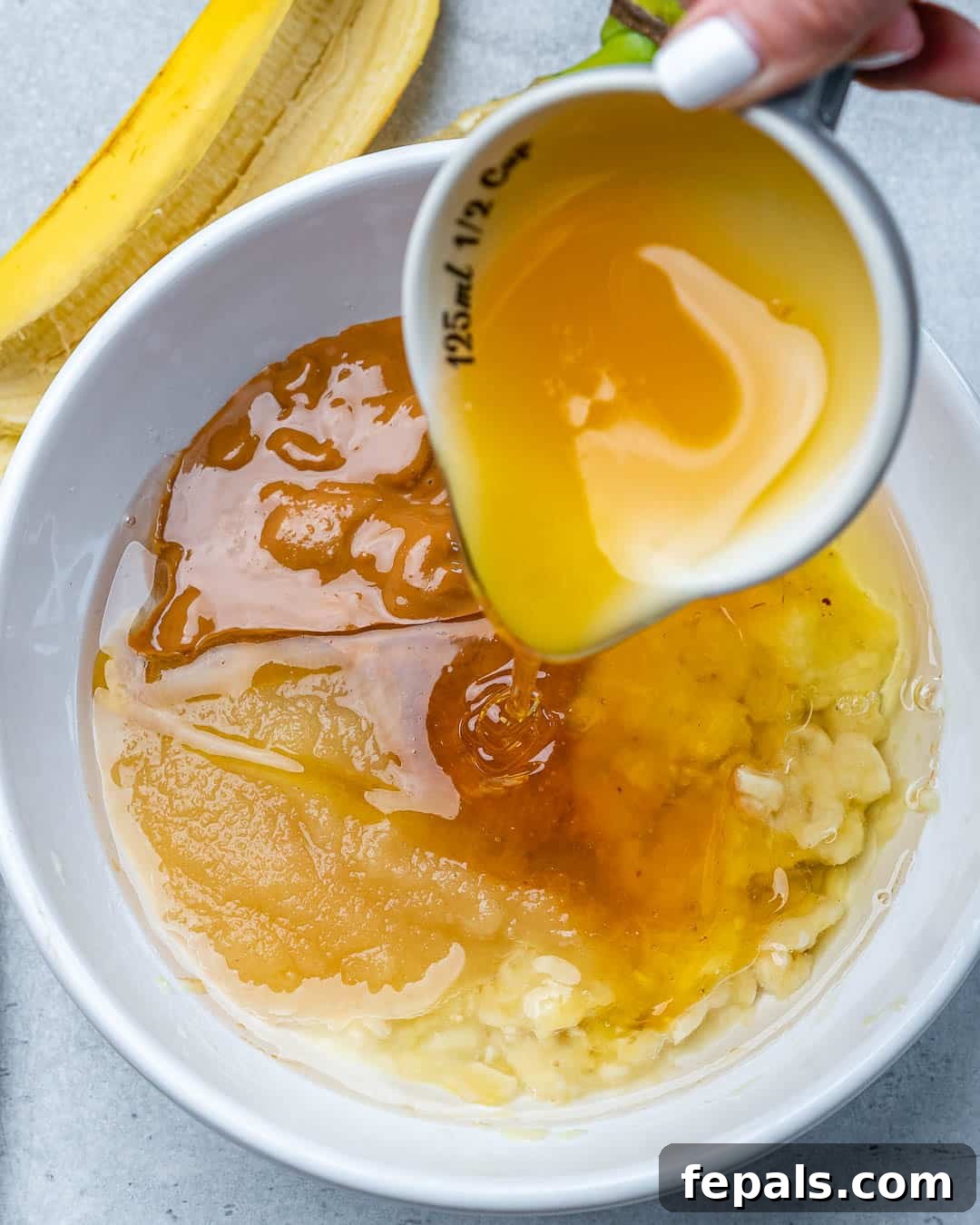 A hand gently pouring golden honey into a bowl filled with other wet ingredients for the muffin batter.