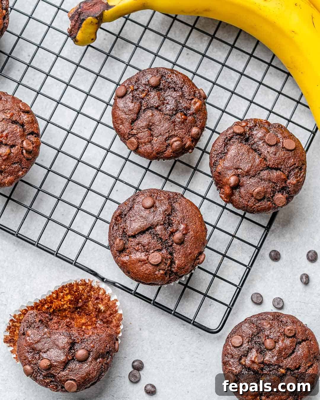Freshly baked chocolate peanut butter banana muffins cooling on a wire rack, with some wrappers already removed.