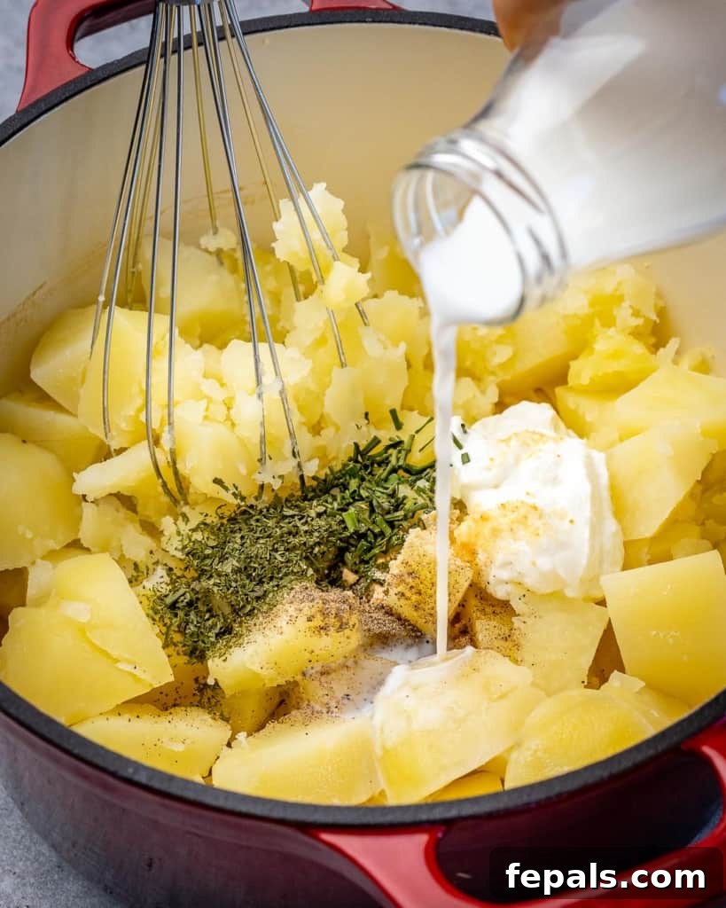 A pot with chunks of potatoes being mixed with milk and seasoning in a red pot.