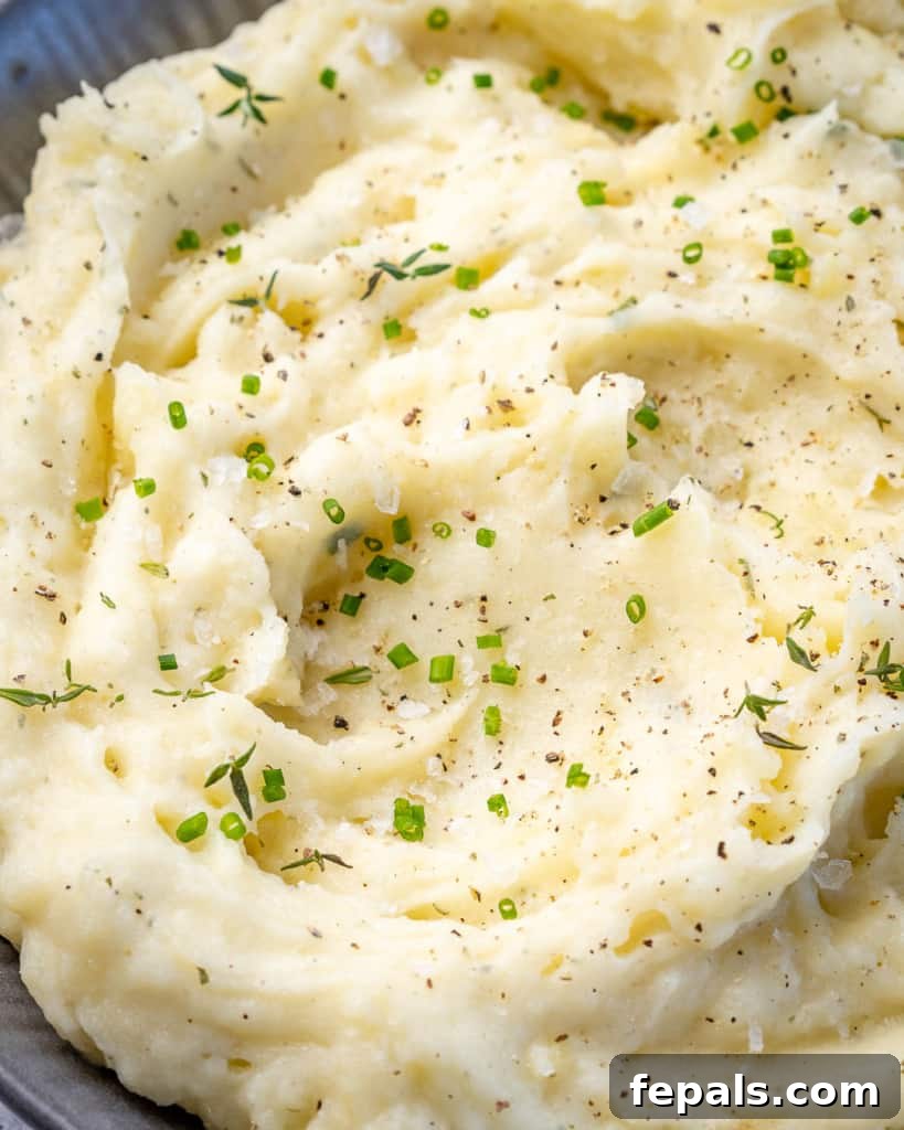 Mashed potatoes in a grey bowl with fresh herb garnish.
