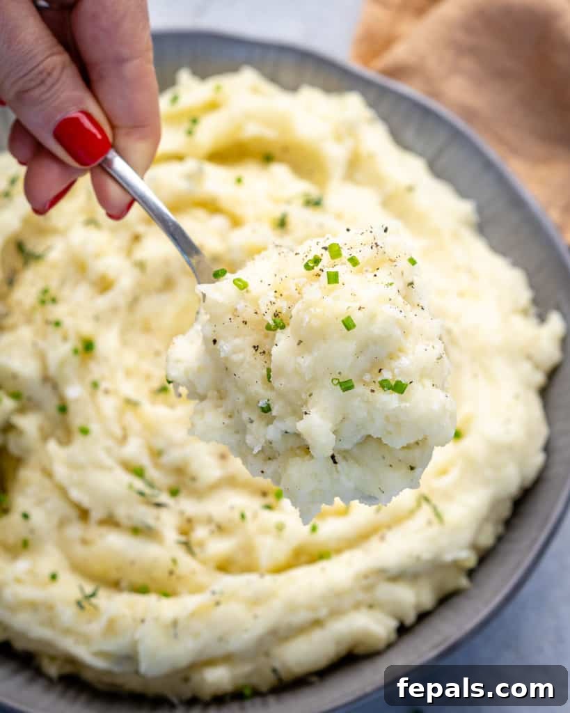 Hand scooping a spoonful of healthy mashed potatoes from a bowl.