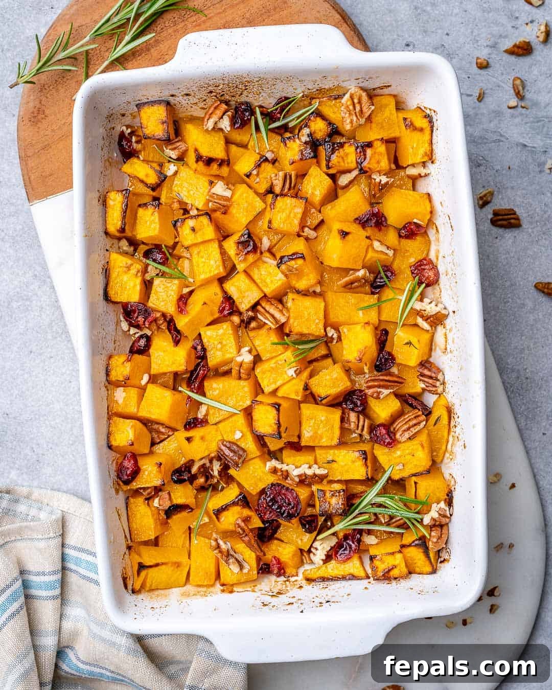 Maple Caramelized Butternut 7 White baking dish filled with beautifully roasted butternut squash, garnished with fresh thyme, pecans, and dried cranberries, ready to serve.