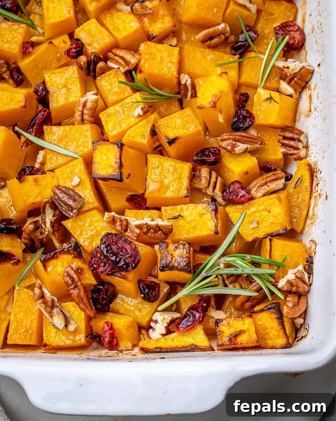 Maple Caramelized Butternut 9 Top view of a white baking dish filled with roasted butternut squash, pecans, and dried cranberries, ready for a festive meal.