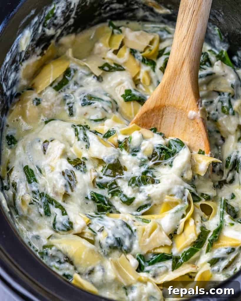 Overhead shot of spoon stirring spinach artichoke dip in a crockpot.
