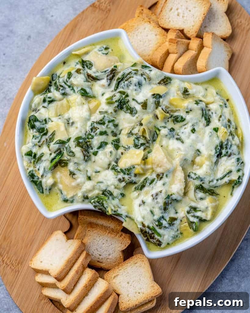 Overhead shot of spinach artichoke dip in a bowl on a wooden board. 