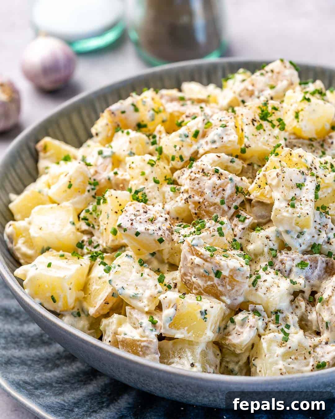 Simple Zesty Mustard Potato Salad 2 Bowl of healthy mustard potato salad with fresh herbs and a hint of a mustard sauce, featuring salt and pepper shakers in the soft background.