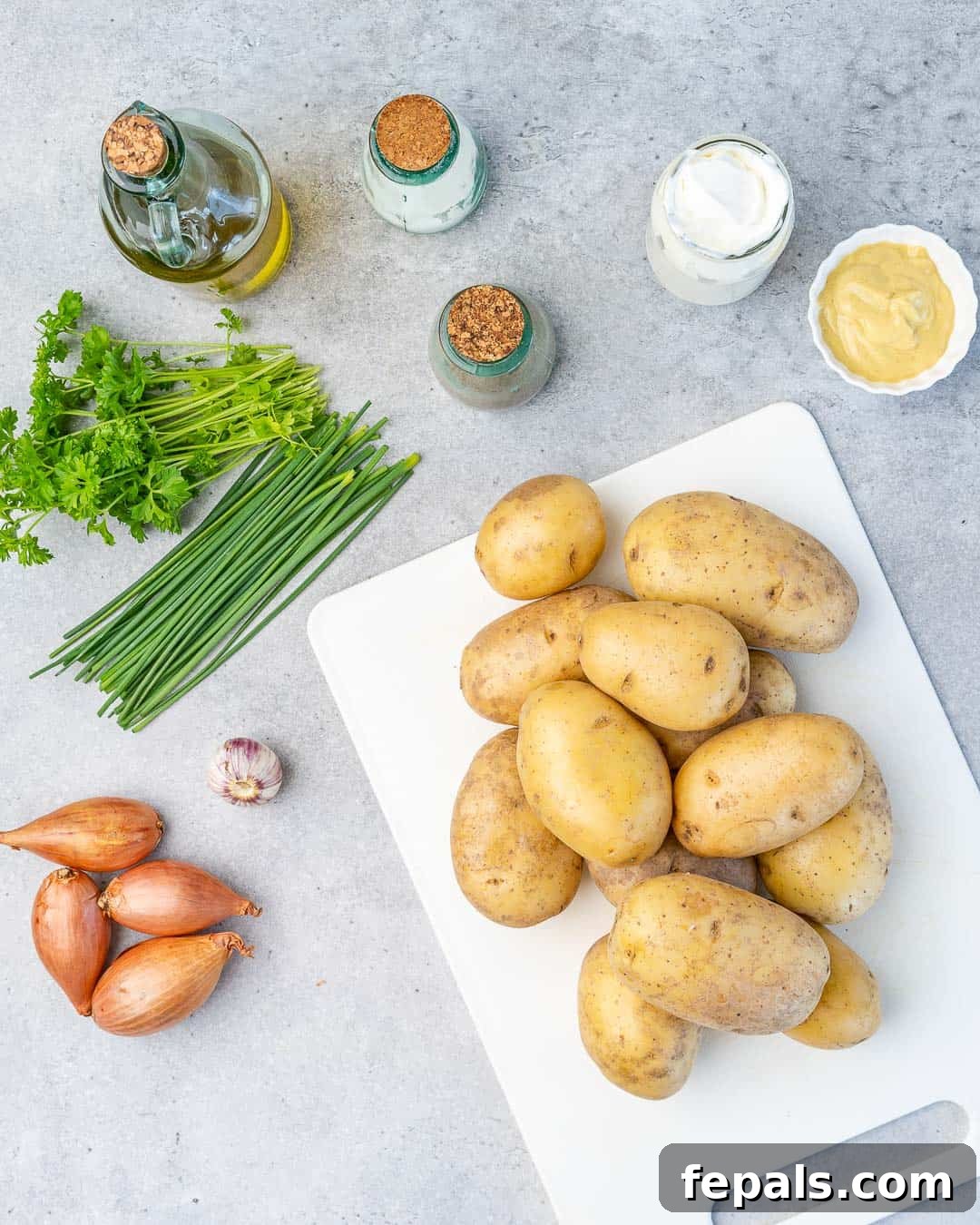 Simple Zesty Mustard Potato Salad 4 A collection of fresh ingredients for healthy mustard potato salad, neatly arranged on a kitchen counter: baby new potatoes, Greek yogurt, Dijon mustard, shallots, garlic, chives, and parsley.