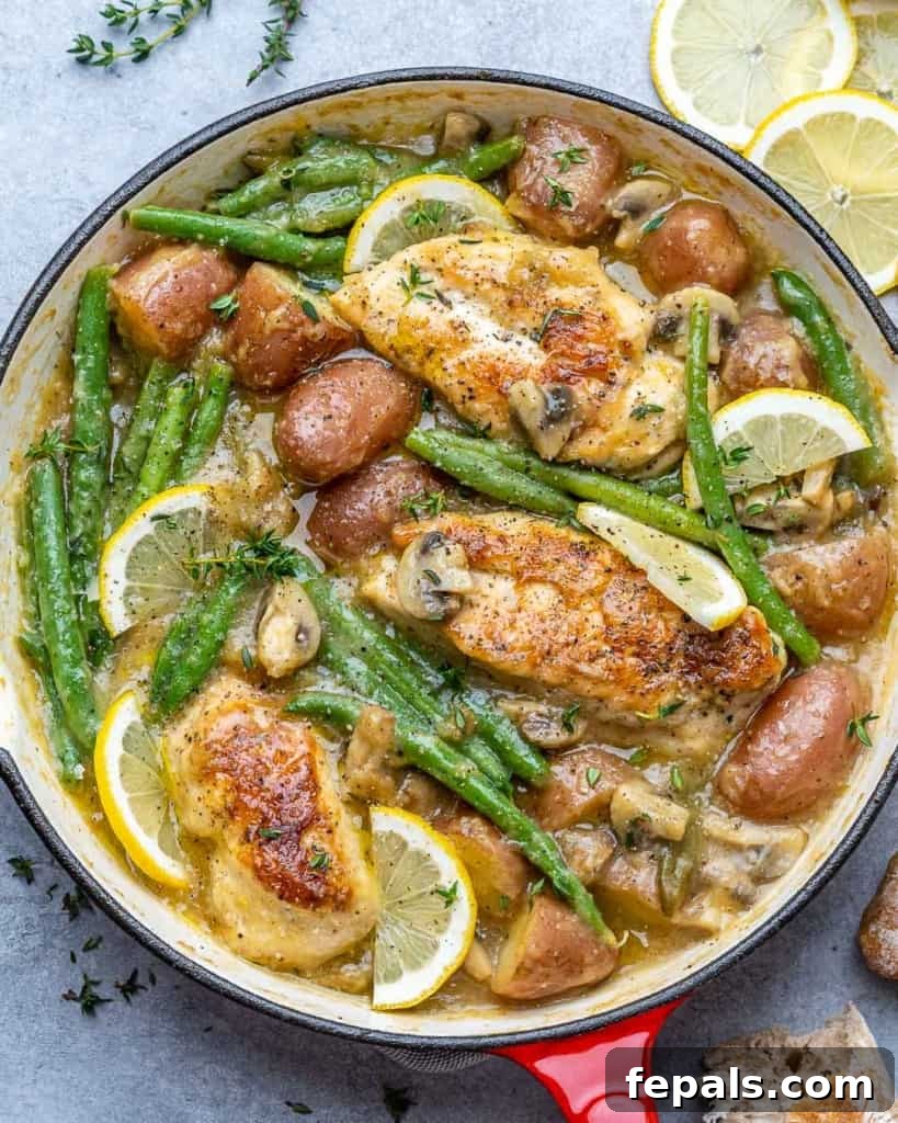 top view chicken skillet with potatoes and green beans topped with lemon garnishes 
