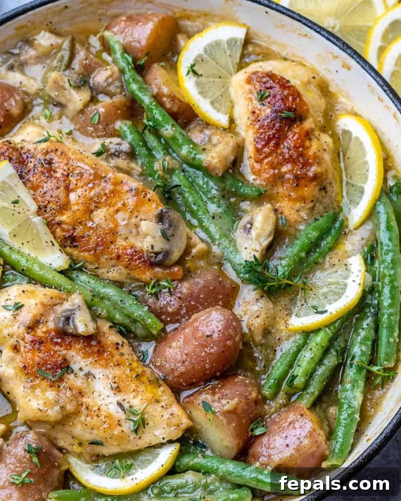 close up chicken potatoes and green beans in a skillet with lemon garnish