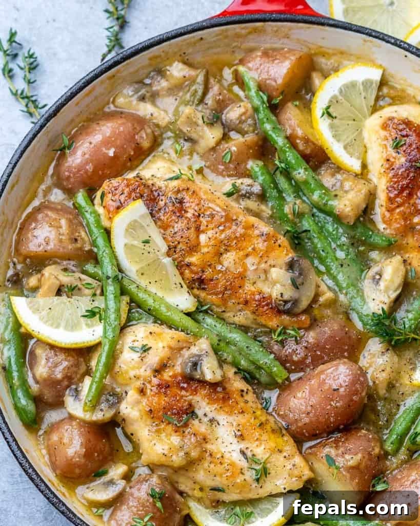 cooked chicken breast in a skillet with potatoes, mushrooms, green beans, and lemon garnishes 