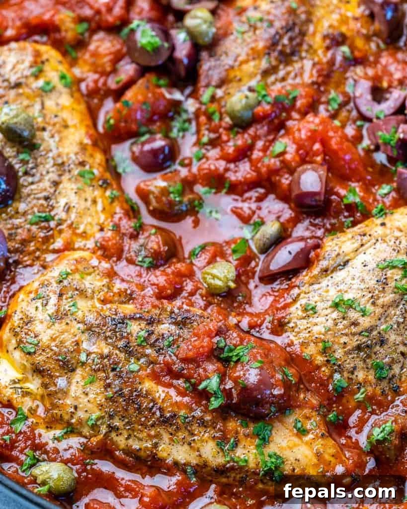 Rustic Chicken Puttanesca 7 close up view of chicken breasts cooked in a red color puttanesca sauce in a skillet