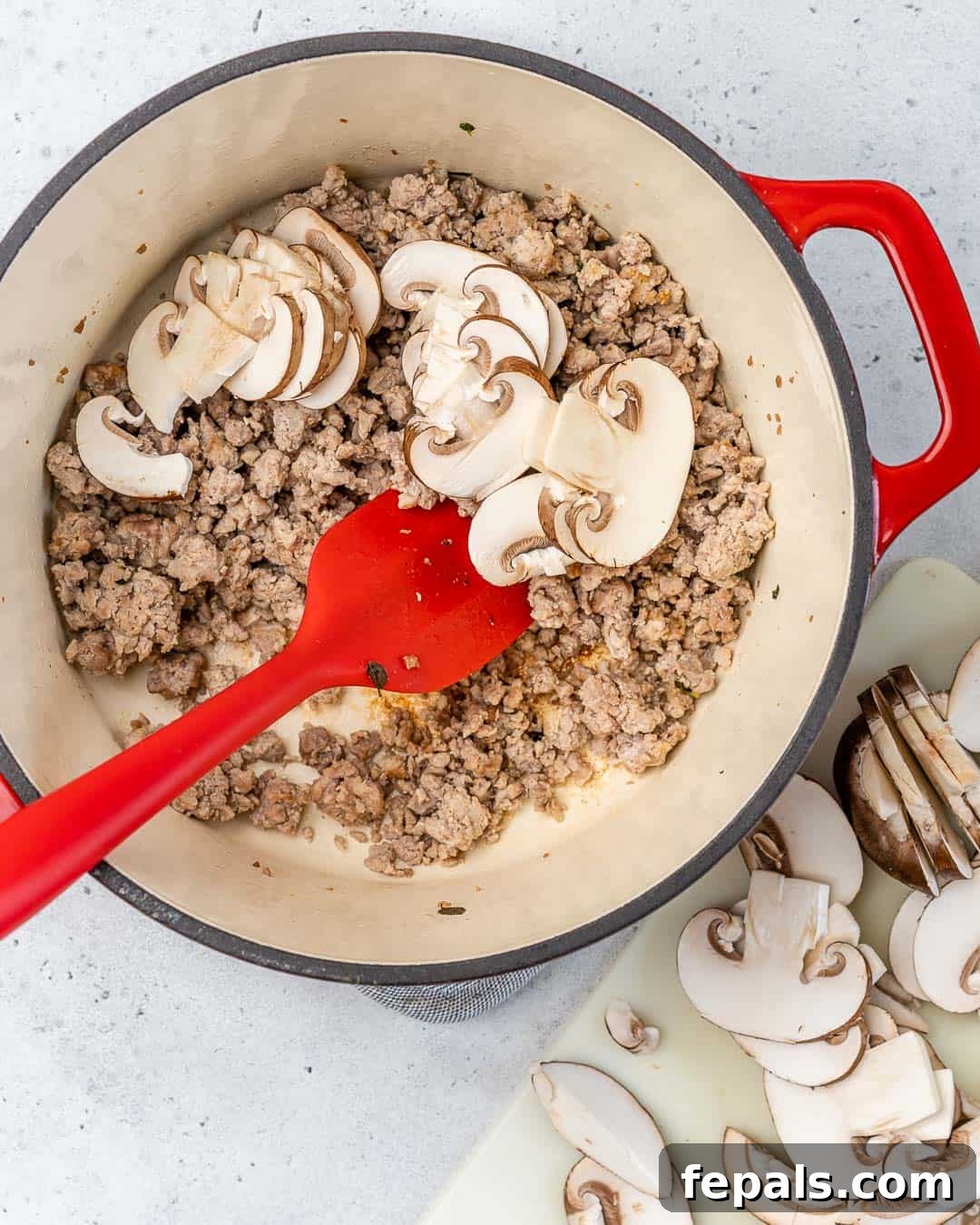 Sautéing Chicken and Mushrooms for Soup Ground chicken and sliced Cremini mushrooms sizzling in a Dutch oven with a spatula.