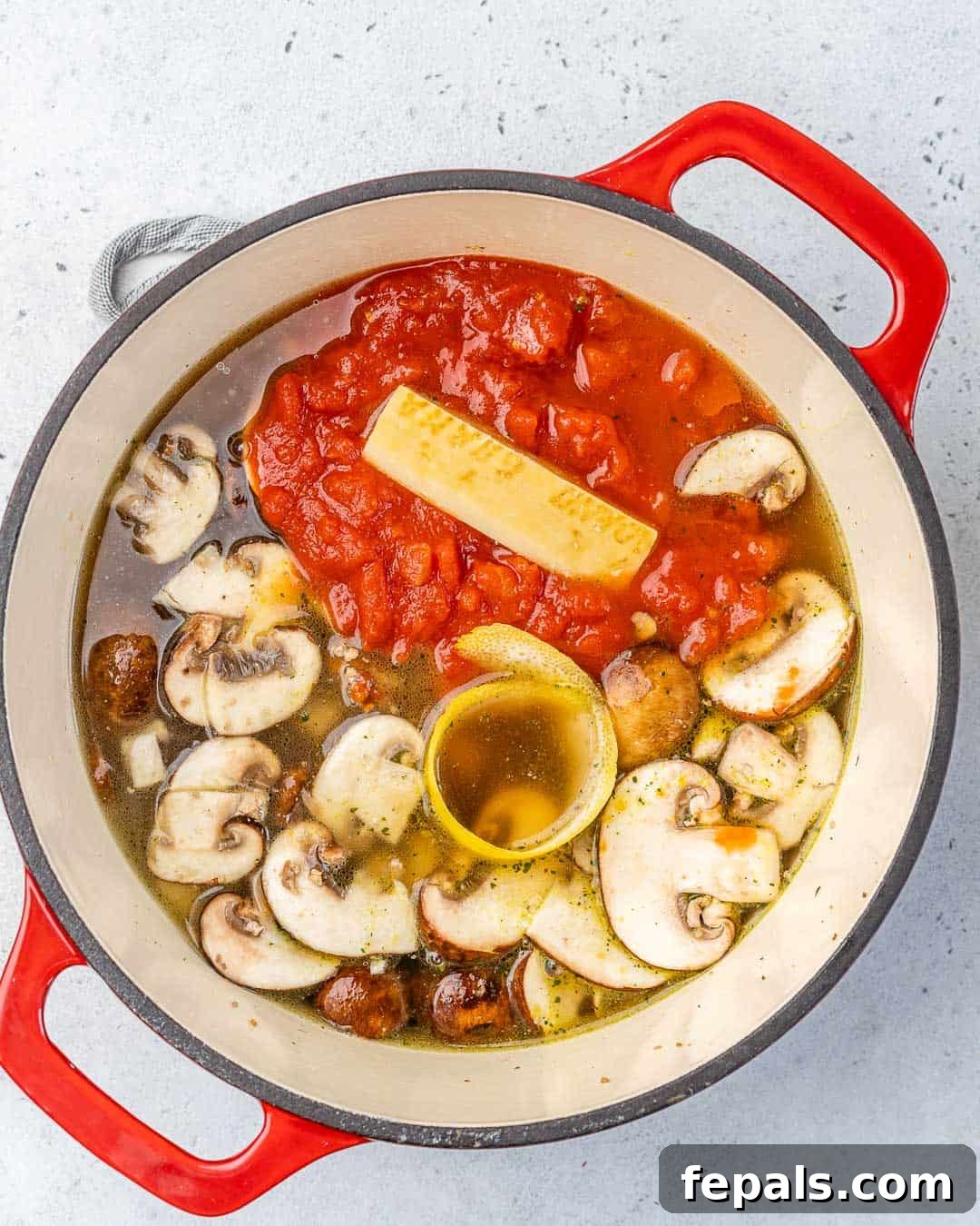 Adding Key Flavors to Orzo Soup Diced tomatoes, Parmesan rind, and lemon zest being added to the pot with chicken and mushrooms.