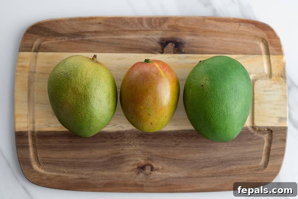 Top view of three ripe mangoes on a wooden cutting board, ready for slicing